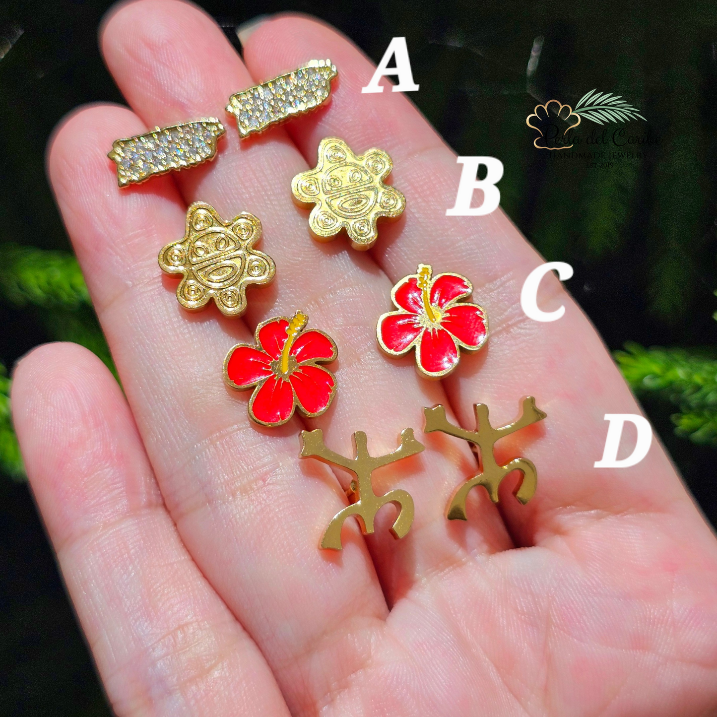 Gold and red floral earrings held in a hand with a green leafy background